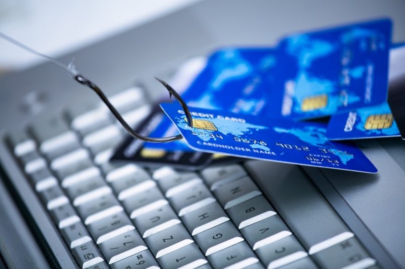 Piles of credit cards with a fish hook on computer keyboard.